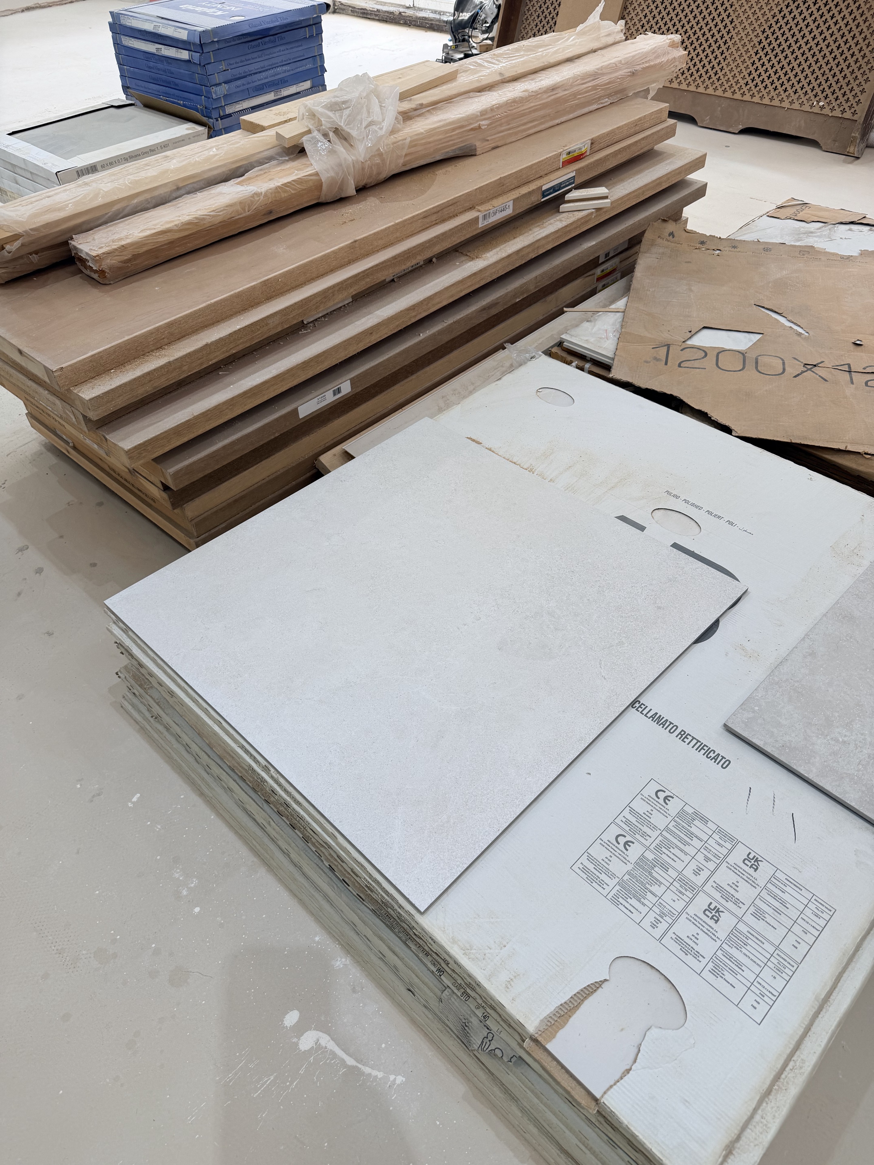 The large pale tile sample that informed the final colour choice, resting on packaging in the house.