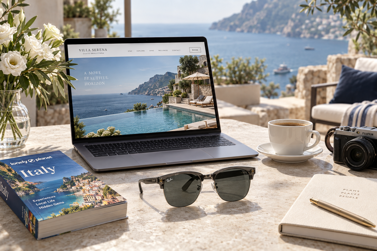An editorial hotel-research scene with a Mediterranean hotel on a laptop, a Lonely Planet guide, white flowers, coffee, sunglasses, notebook and camera beside a sea-view terrace.
