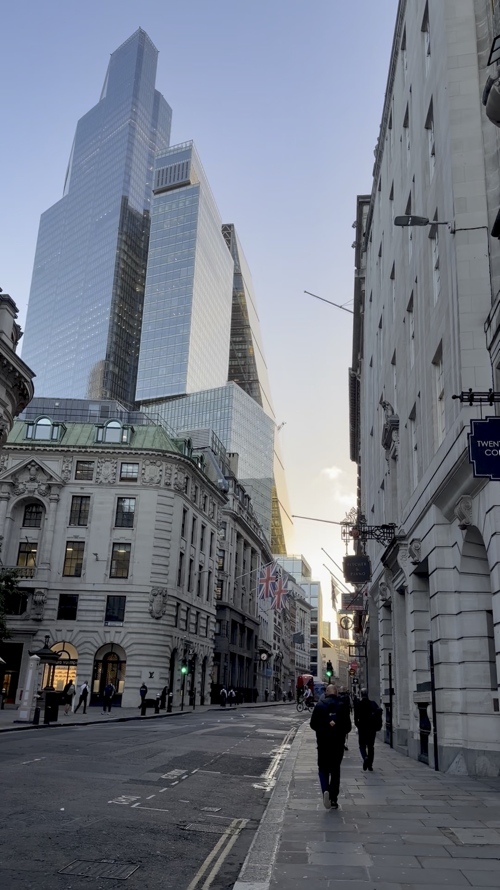 A City of London street with pedestrians, historic stone buildings and modern glass towers, from Emma-Kate’s own footage.
