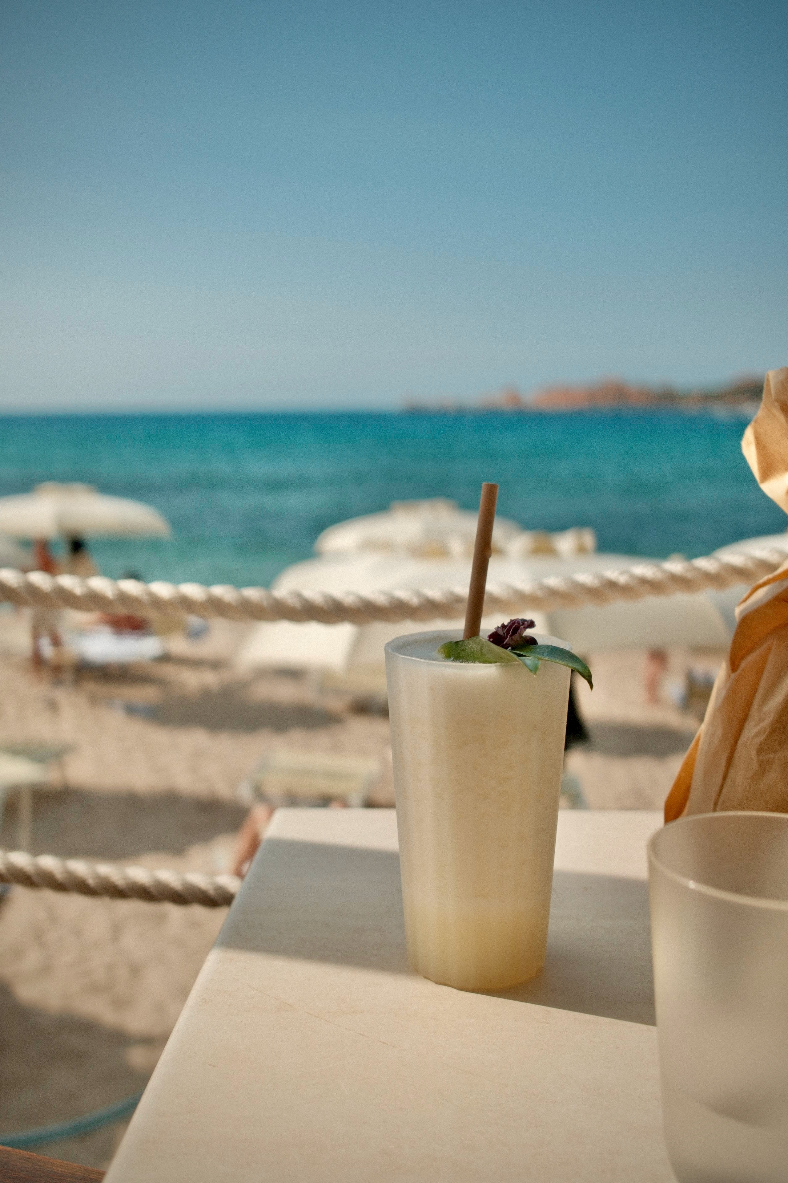 Emma-Kate’s photograph of a drink at a beach-side table, with parasols and the sea beyond.